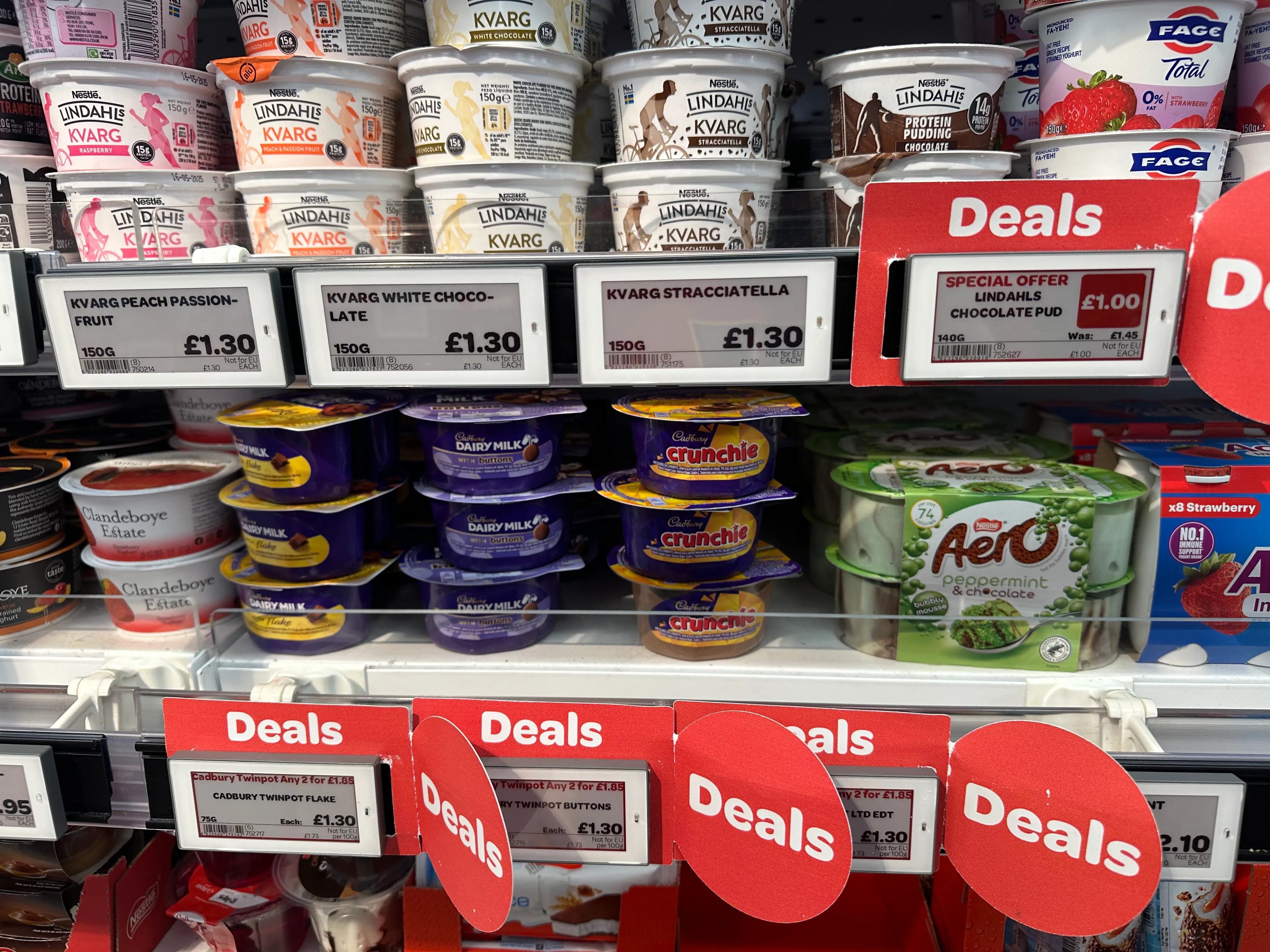 A row of yoghurts on a shelf in a convenience store, with some Electronic Shelf Labels attached, displaying the price of each item